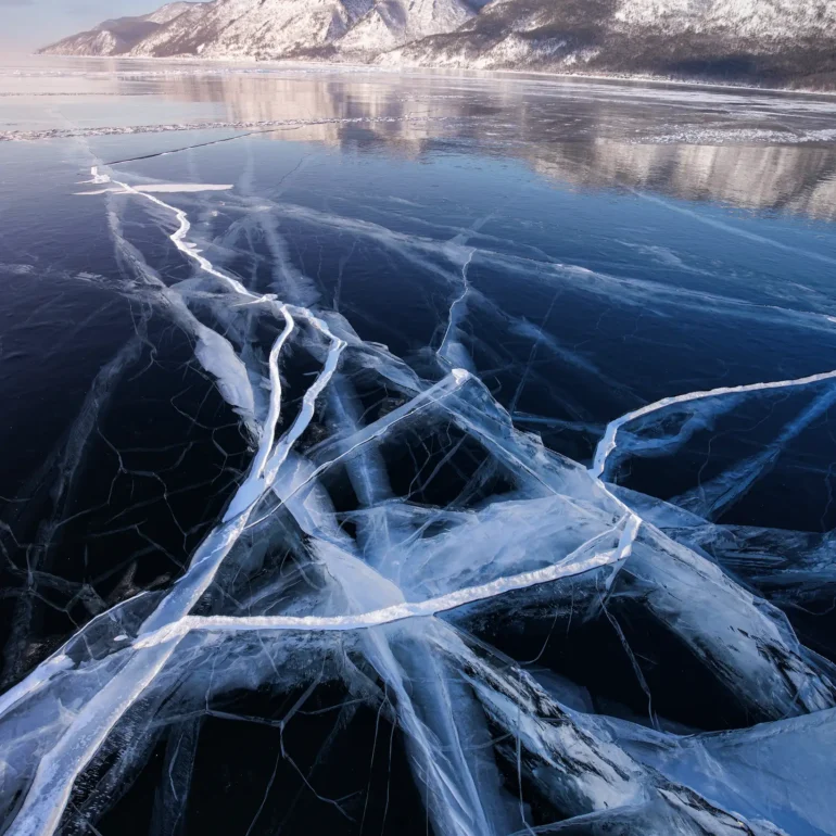 Natural cracked ice patterns forming geometric shapes across the frozen surface of Lake Baikal during winter in Siberia, Russia.