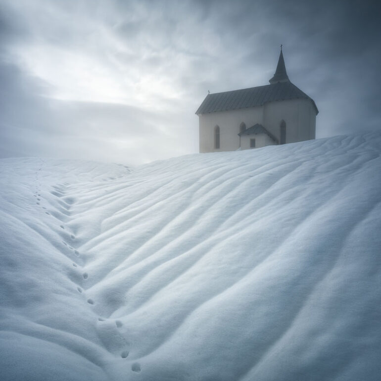 Santa Barbara Church surrounded by snow and illuminated by magical winter light in Comelico, Belluno, in the Italian Dolomites.