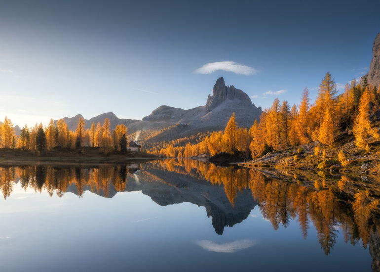 The golden larch forests surrounding Lago Federa reflecting the majestic Becco di Mezzodì during a colourful autumn sunrise in the Italian Dolomites.