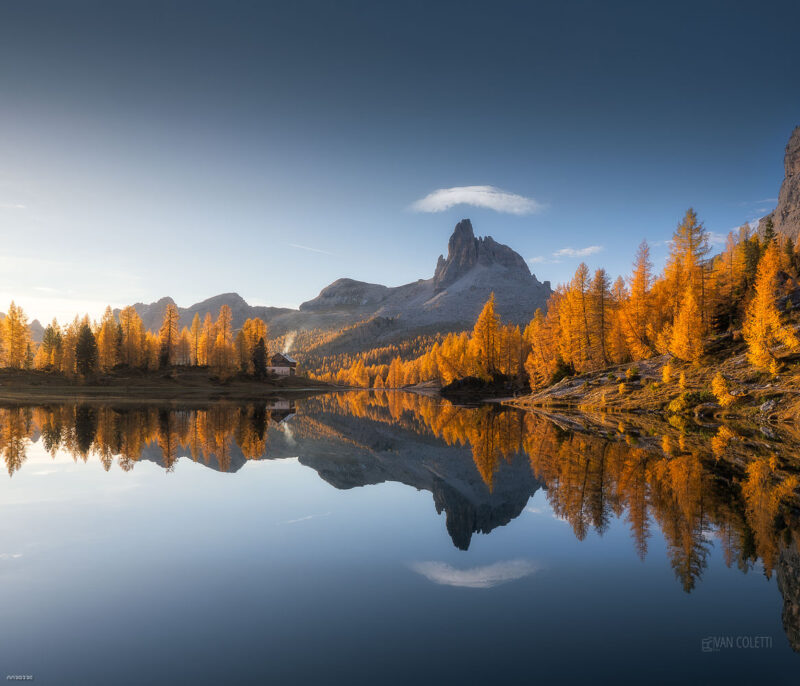 The golden larch forests surrounding Lago Federa reflecting the majestic Becco di Mezzodì during a colourful autumn sunrise in the Italian Dolomites.