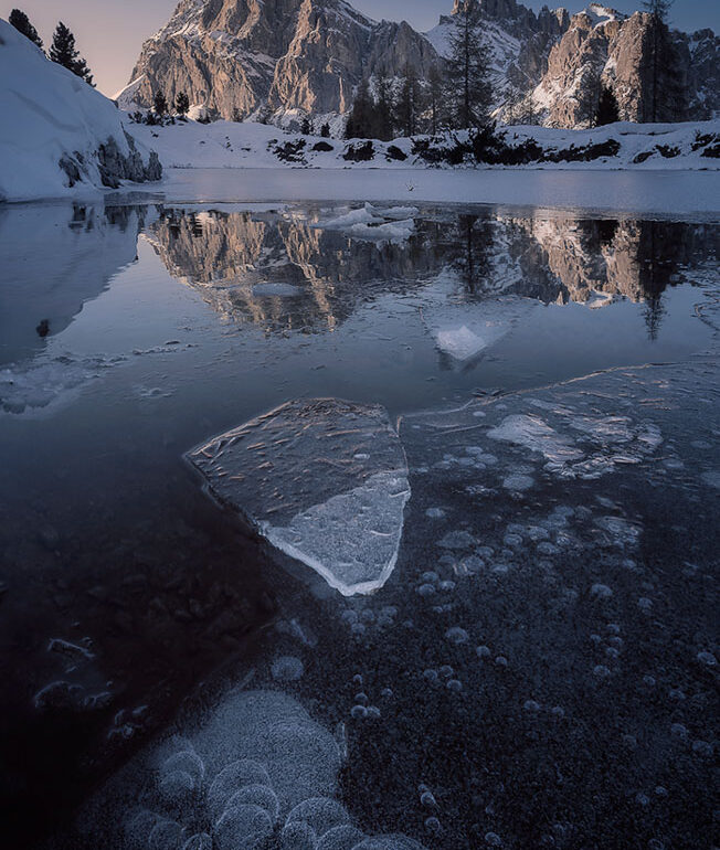 The first ice forming on Lake Limides beneath the towering Lagazuoi at sunset in the UNESCO-listed Italian Dolomites near Cortina d