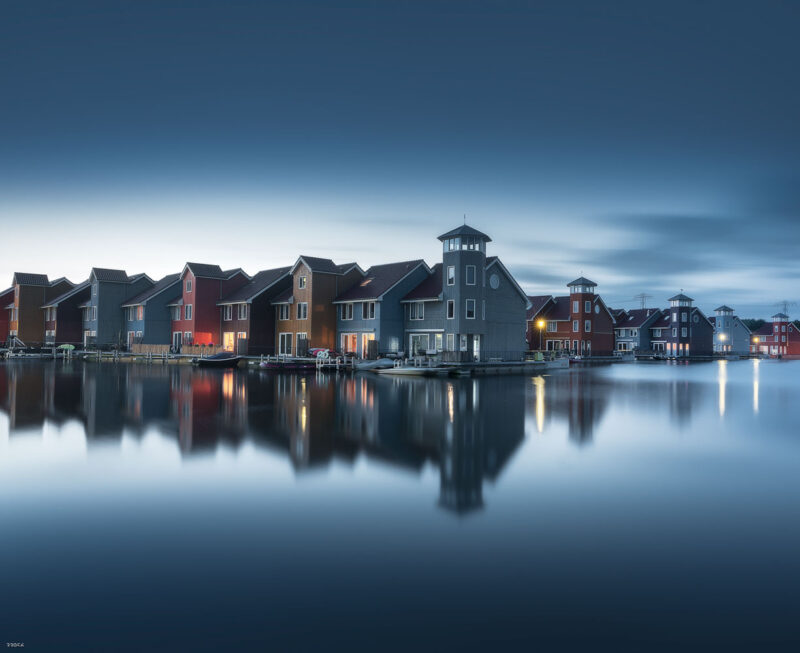 Colourful waterfront houses reflected in the calm harbor during the blue hour in Groningen, the Netherlands.