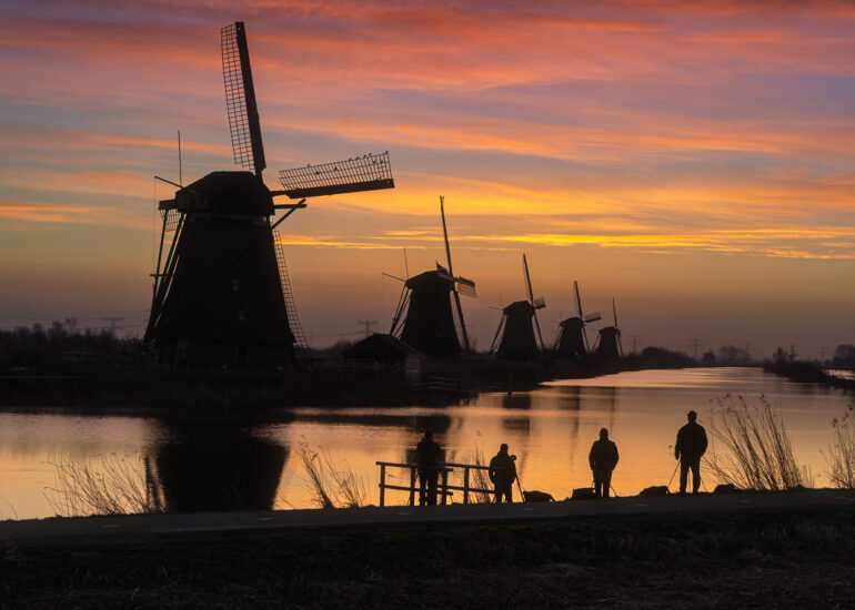 Historic windmills of Kinderdijk reflected in calm water during a golden sunrise in the Netherlands, a UNESCO World Heritage Site.