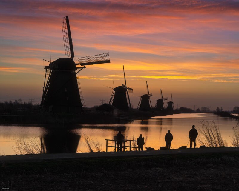 Historic windmills of Kinderdijk reflected in calm water during a golden sunrise in the Netherlands, a UNESCO World Heritage Site.