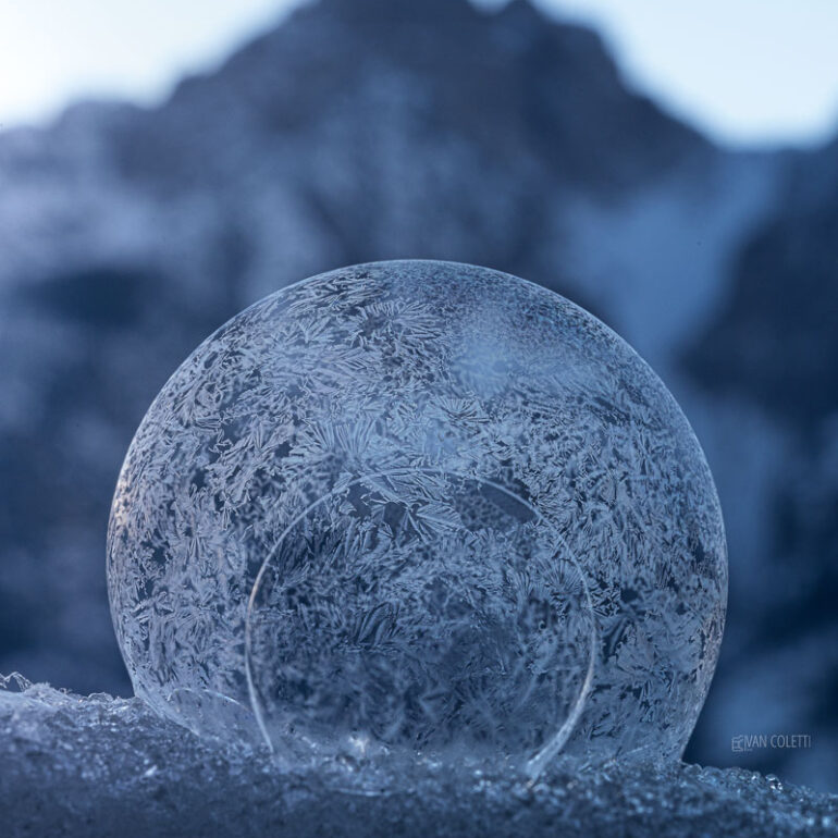 Intricate crystal patterns forming across a frozen soap bubble during a freezing winter morning.