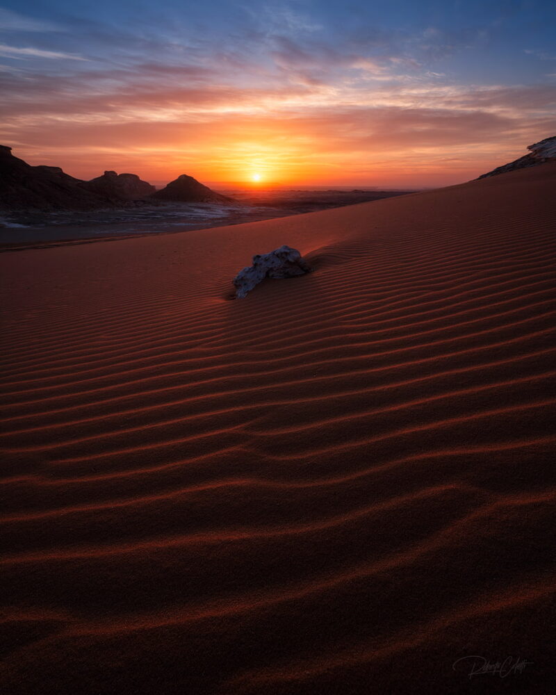 White chalk formations rising from red desert sand beneath a colourful sunrise sky in Egypt