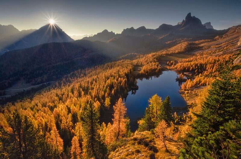 Golden autumn larches surrounding Lago Federa as the first rays of sunrise emerge behind Monte Antelao near Cortina d