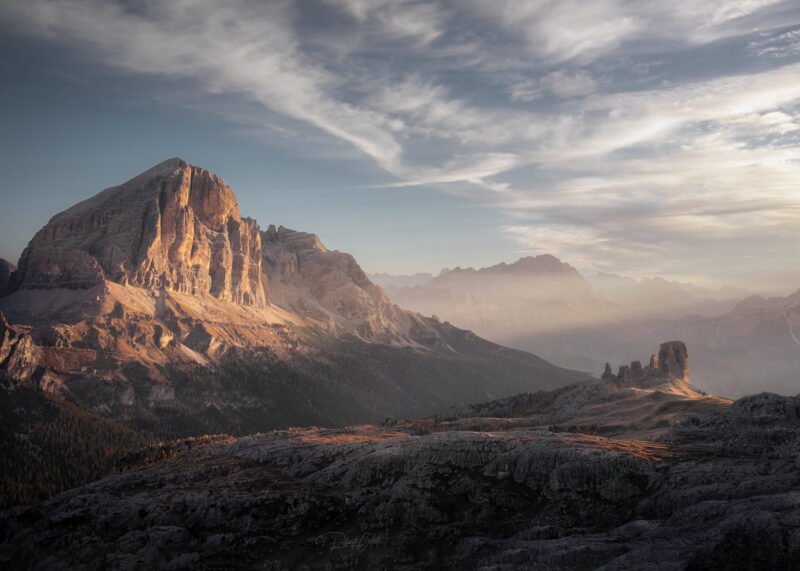 Sunrise illuminating the Cinque Torri with the majestic Tofane rising in the background above an alpine meadow in the Italian Dolomites.