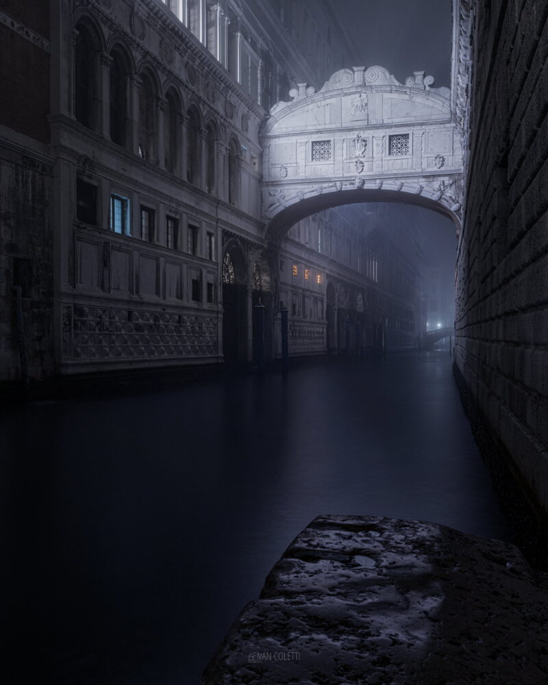 The illuminated Bridge of Sighs spanning a Venetian canal at night in Venice, Italy, surrounded by historic architecture and shimmering reflections.