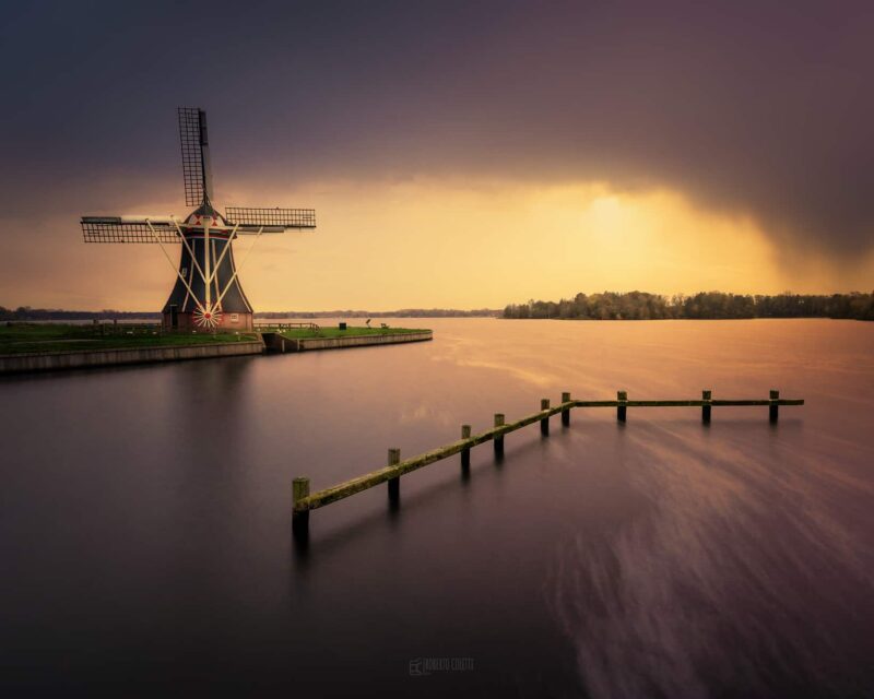 Historic Dutch windmill reflected in calm water during sunset in Groningen, the Netherlands.