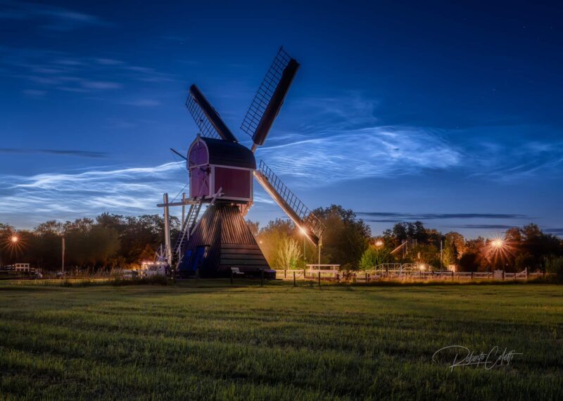 Historic red Dutch windmill in Zuilen, Utrecht, illuminated beneath spectacular noctilucent clouds on a summer night in the Netherlands.