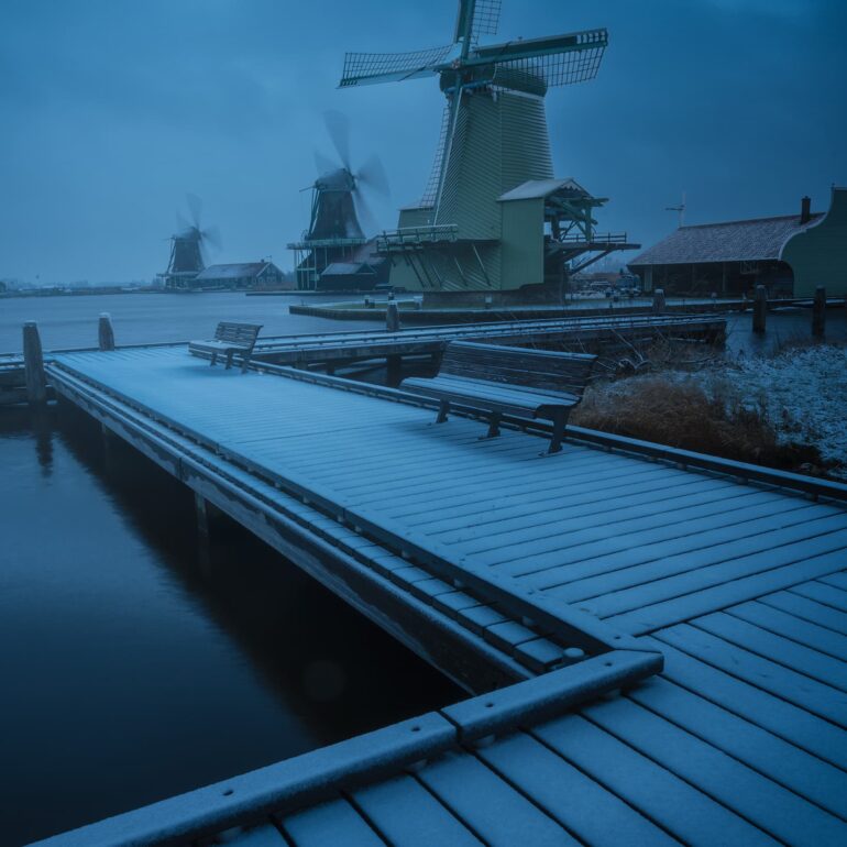 Historic Dutch windmills covered by the first snowfall during the blue hour at dawn in Zaanse Schans, the Netherlands.