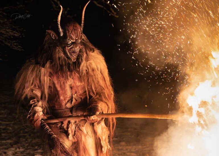 Krampus performer emerging from the darkness during a dramatic winter night celebration in the Italian Dolomites.