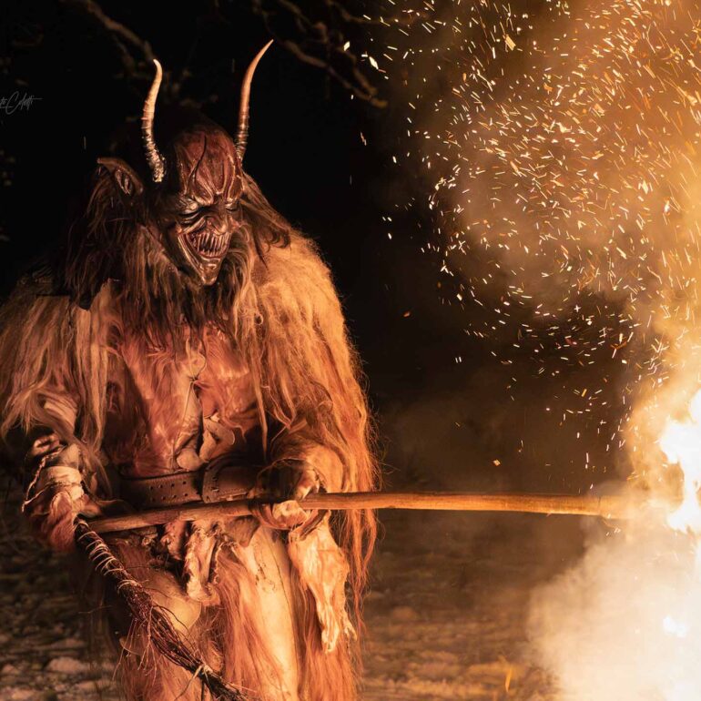 Krampus performer emerging from the darkness during a dramatic winter night celebration in the Italian Dolomites.
