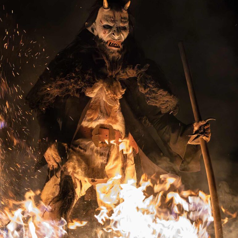 Krampus surrounded by flying sparks and fire during a dramatic winter night festival in Italy.