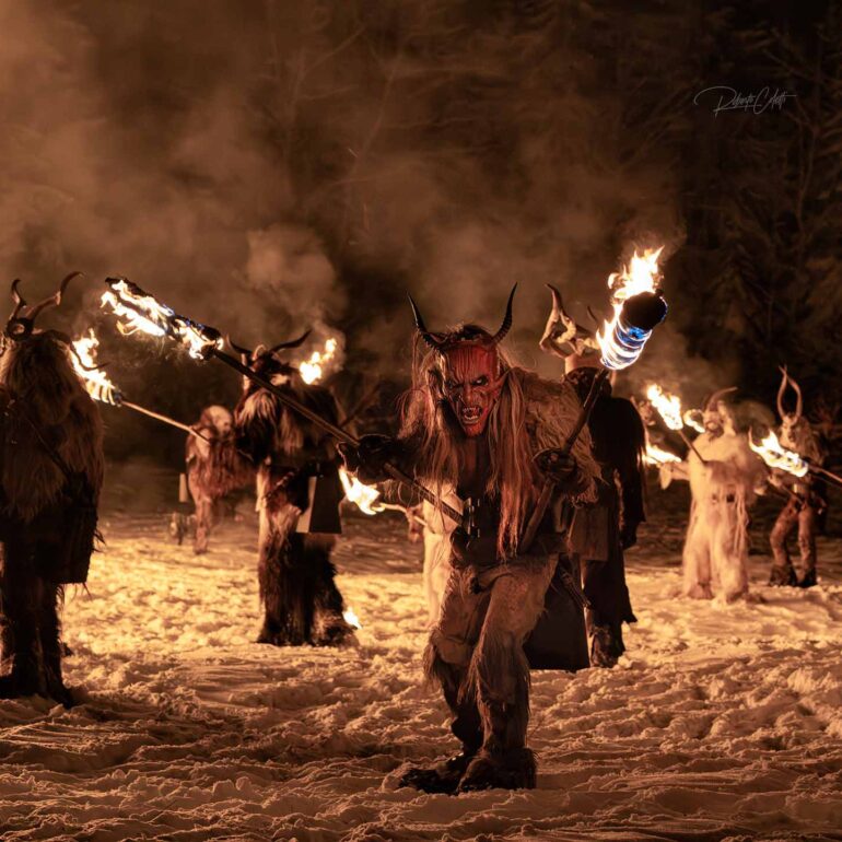 Krampus swinging heavy chains while walking through fire during a traditional alpine festival.