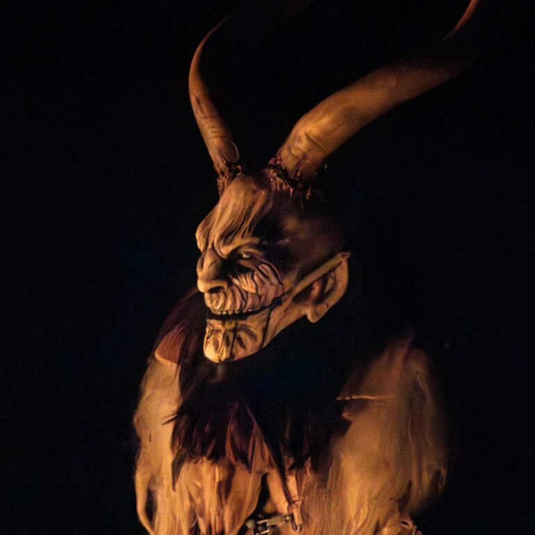 Close-up of a traditional wooden Krampus mask illuminated by flames during a night parade in Italy.