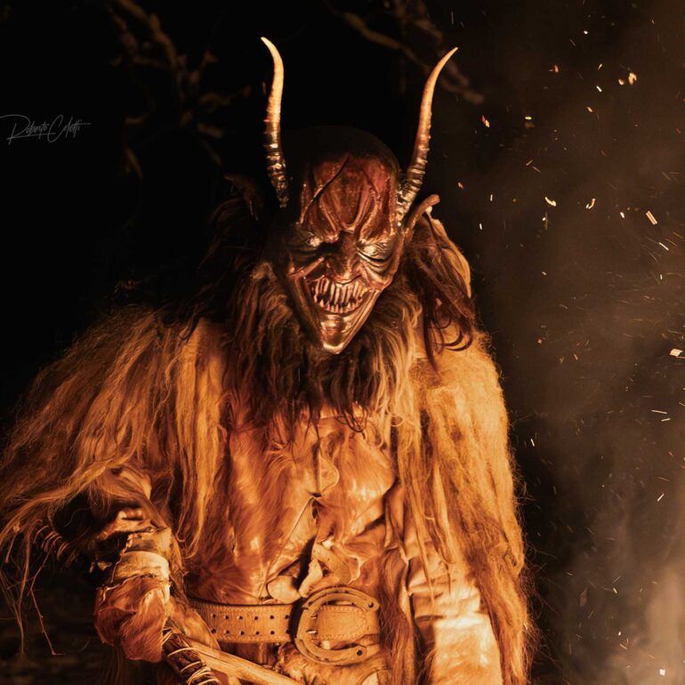 Krampus parade with fire and traditional costumes during a December night in northern Italy.