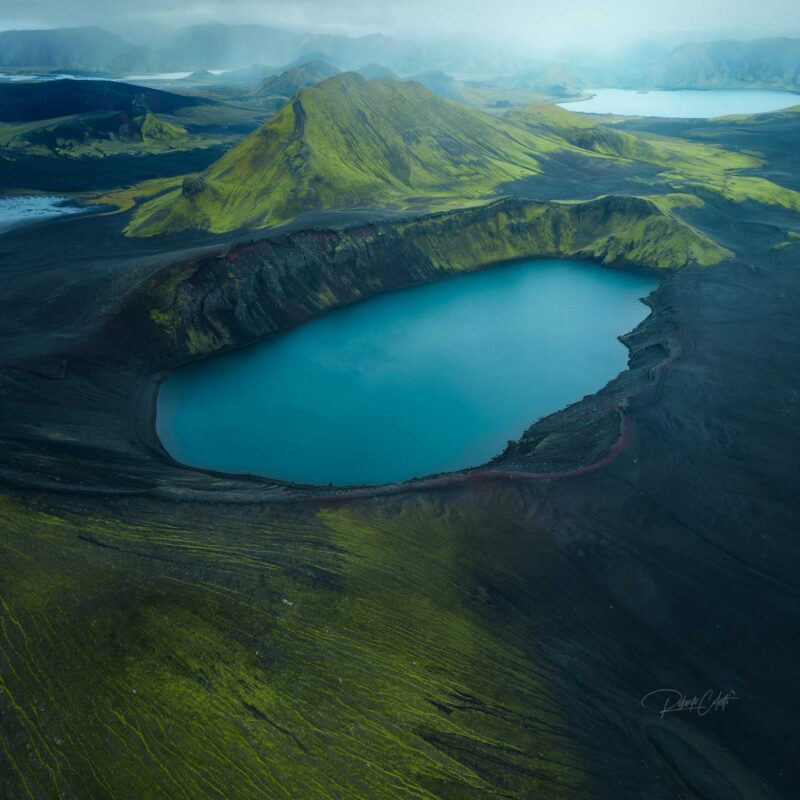 Green volcanic crater overlooking a vivid blue lake in Iceland during a misty autumn day