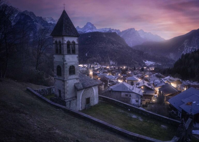 The hilltop church of Nebbiù di Cadore overlooking the village during a winter blue hour in the Italian Dolomites.