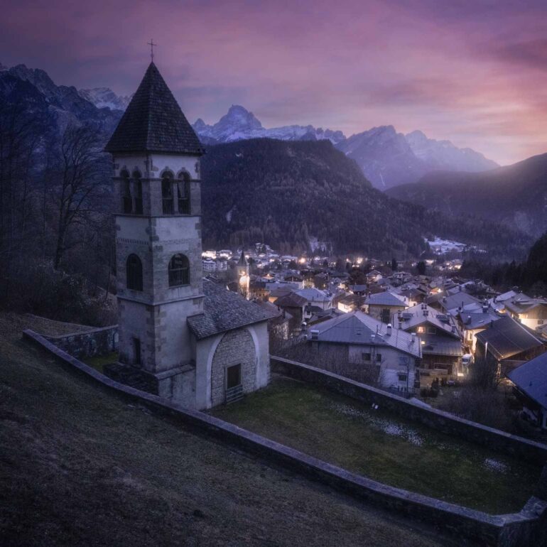 The hilltop church of Nebbiù di Cadore overlooking the village during a winter blue hour in the Italian Dolomites.