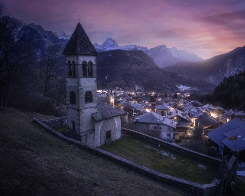 The hilltop church of Nebbiù di Cadore overlooking the village during a winter blue hour in the Italian Dolomites.