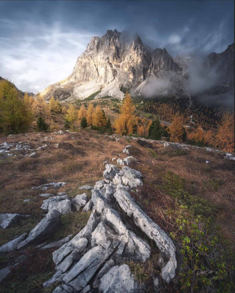 Colorful autumn landscape at Passo Falzarego in the Italian Dolomites, with dramatic clouds drifting above rugged limestone rocks.