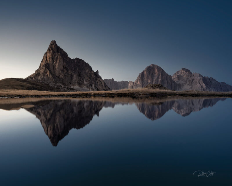 Blue hour reflections of Ra Gusela and the Tofana massif in a mountain pond at Passo Giau in the Italian Dolomites.