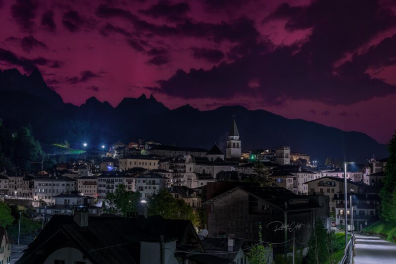 Rare Aurora Borealis above the historic town of Pieve di Cadore in the Italian Dolomites, Italy, during a crystal-clear night.