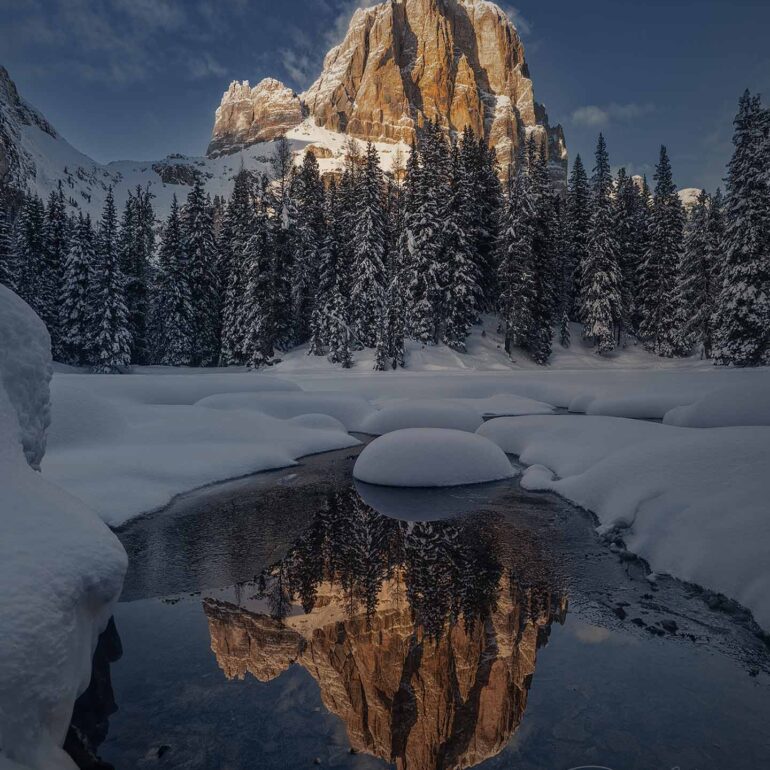 Tofana de Rozes mountain reflected in the small lake of Bai de Dones in the Dolomites, Italy, during a winter sunset.