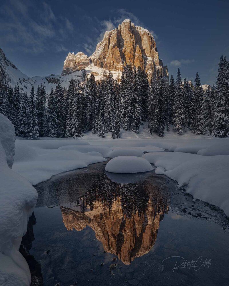 Tofana de Rozes mountain reflected in the small lake of Bai de Dones in the Dolomites, Italy, during a winter sunset.