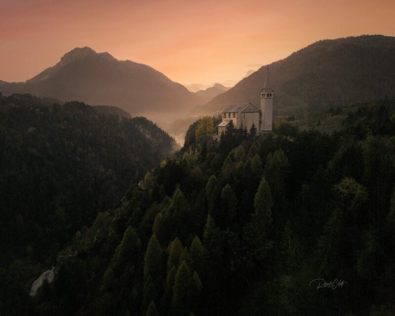 Colorful autumn sunset over Valle di Cadore in the Italian Dolomites, with the hilltop Church of San Martino overlooking the village.