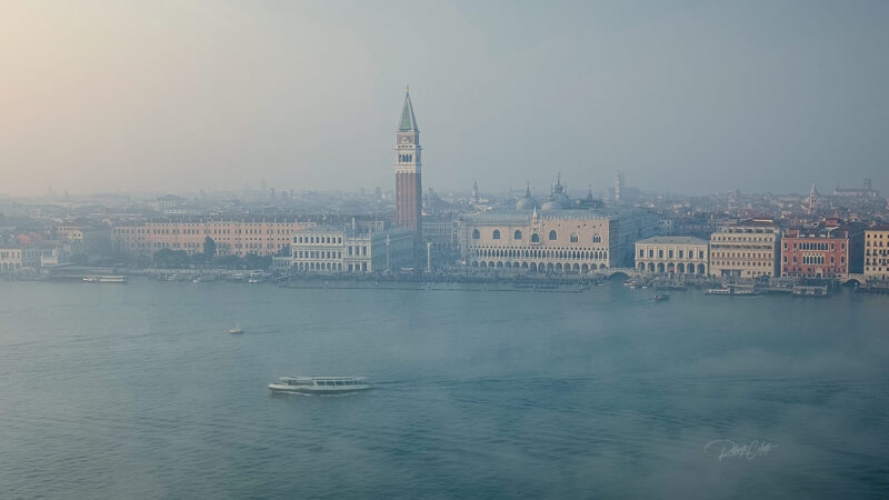 Aerial view of St. Marco Square in Venice, Italy, on a foggy morning, with the iconic basilica and bell tower emerging from the mist