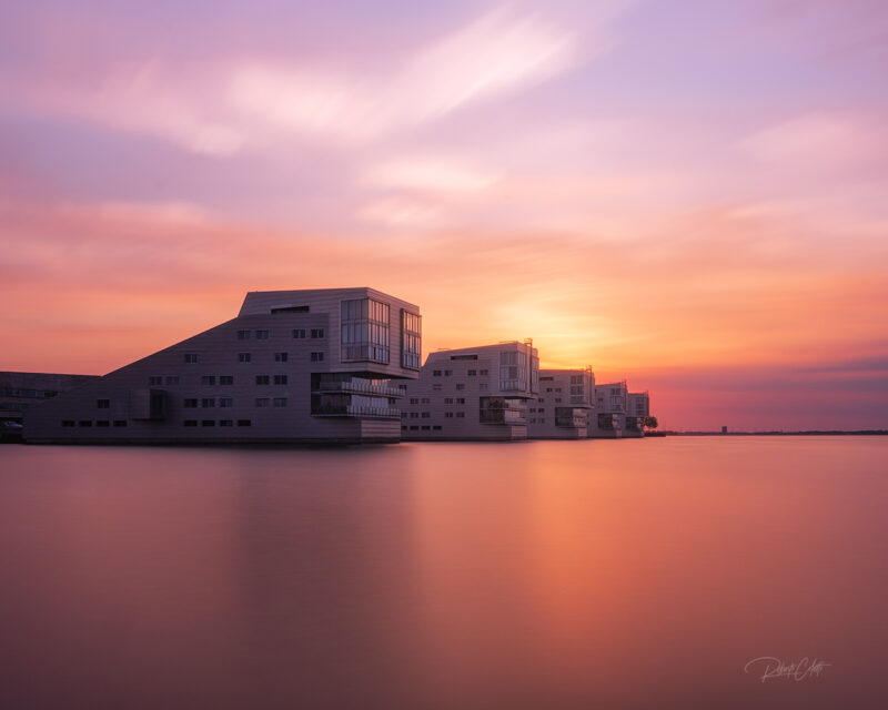 Modern waterfront architecture reflected on Lake Gooimeer beneath a dramatic red sunset in the Netherlands.
