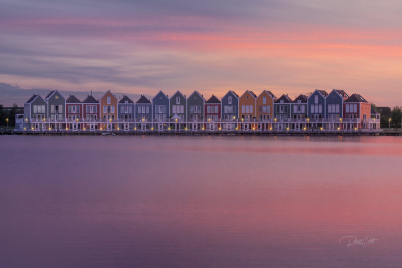 Colorful waterfront houses reflected in a calm lake at sunset in Houten, the Netherlands.