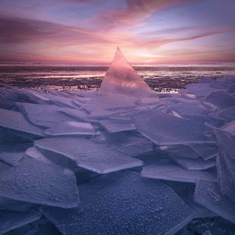 Ice floes along the North Sea coast in the Netherlands glowing beneath a spectacular colorful sunrise on a freezing winter morning.