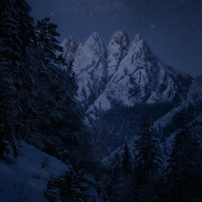 Home Snow-covered mountain peaks beneath a star-filled winter sky in Friuli Venezia Giulia, Italy.