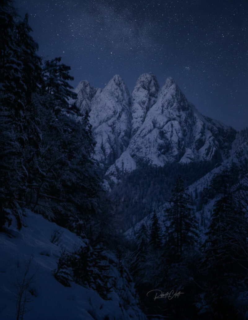 Snow-covered mountain peaks beneath a star-filled winter sky in Friuli Venezia Giulia, Italy.