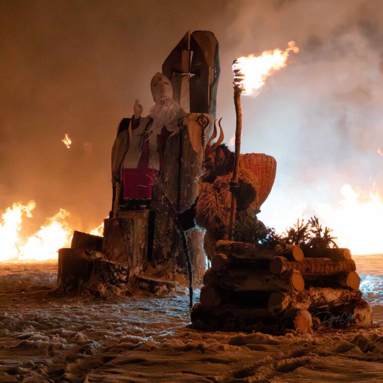 Traditional Krampus parade during the St. Nicholas celebration in Italy, with wooden masks, fire, sparks and dramatic winter atmosphere.