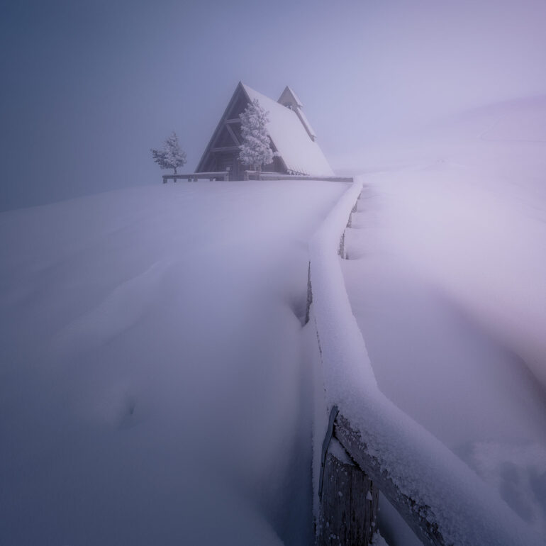 The snow-covered chapel of Passo Giau glowing in the warm light of sunset after a fresh snowfall in the Italian Dolomites.