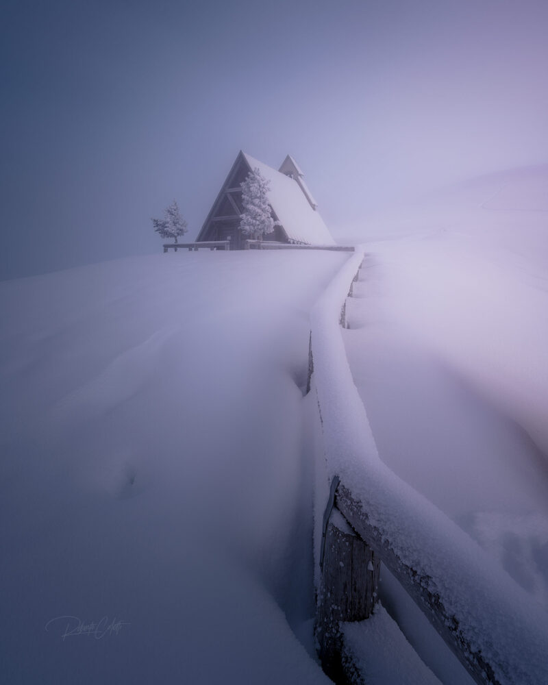 The snow-covered chapel of Passo Giau glowing in the warm light of sunset after a fresh snowfall in the Italian Dolomites.