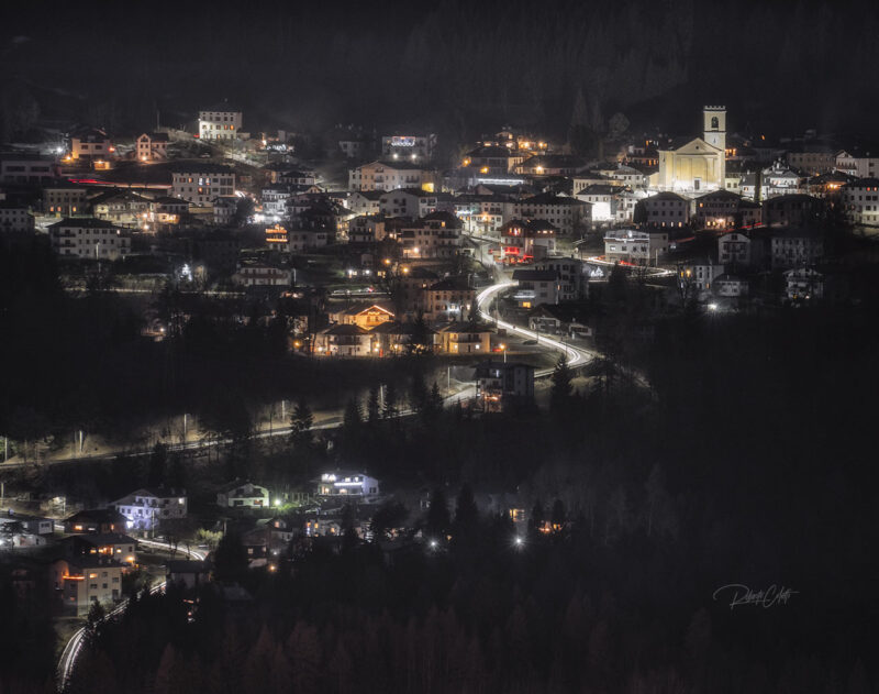 Night view of Pozzale di Cadore from Vedorcia Mountain, with the warm village lights glowing beneath the Dolomites in Italy.