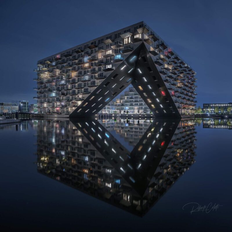 Night view of the iconic Sluishuis residential complex in Amsterdam, showcasing its contemporary architecture reflected on the water in the Netherlands.