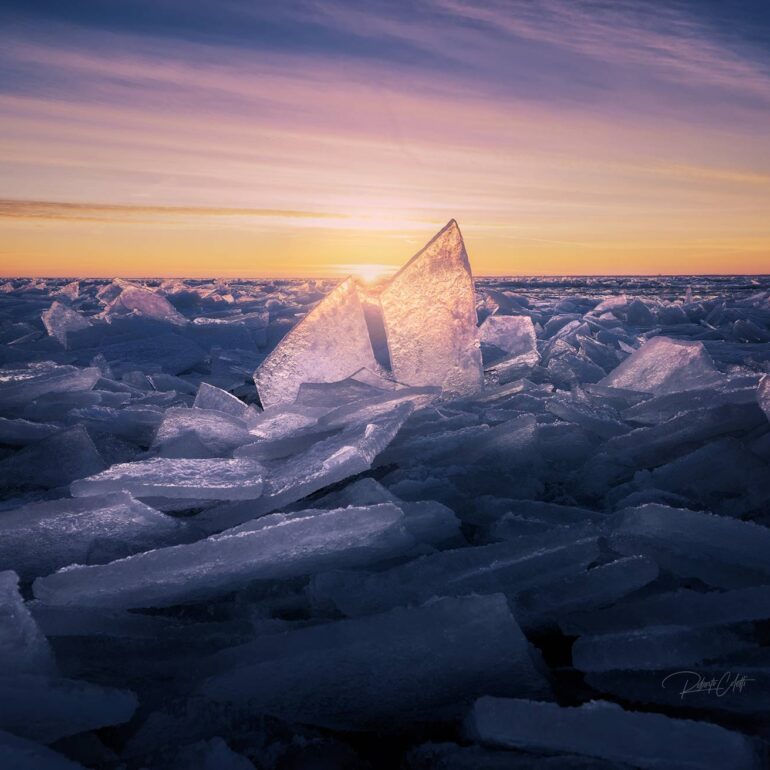 Ice floes along the North Sea coast in the Netherlands at sunrise during a freezing winter morning, illuminated by soft golden light.