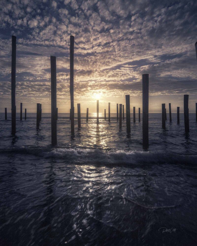 Sunset at Palendorp, the Netherlands, where high tide creates striking geometric patterns among the historic wooden posts along the North Sea coast.